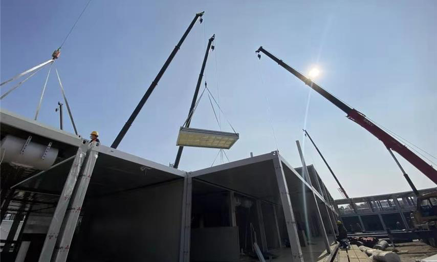 截至1月30日中午12時，武漢火神山醫院項目場地平整、砂石回填、HDPE膜鋪設全部完成，基礎混凝土澆筑完成95％；集裝箱板房進場、改裝、吊裝正快速推進。管線溝槽開挖、埋設級回填完成50％；污水處理間設備吊裝完成，管道安裝完成60％；調蓄水池HDPE膜開始鋪設。圖為住院樓板房吊裝現場。