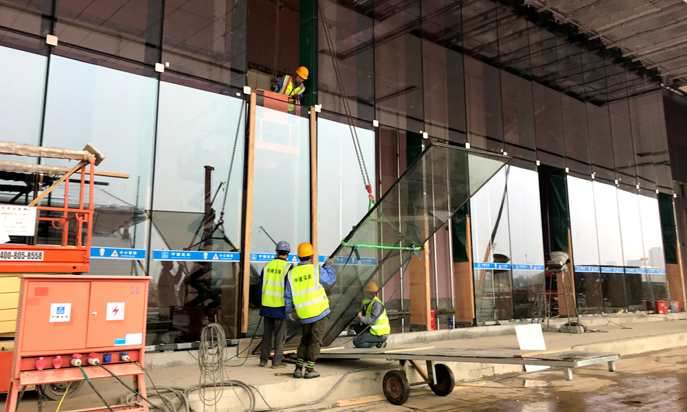 整個會議中心由鋼結(jié)構(gòu)支撐，鋼結(jié)構(gòu)外面全包裹著玻璃幕墻，8千余塊玻璃均為“量身定做”，有獨立編號。圖為4月13日，中建裝飾建筑工人正在吊裝FS2底層坐式全玻幕墻。（國務(wù)院國資委網(wǎng)站 李子紅 攝）
