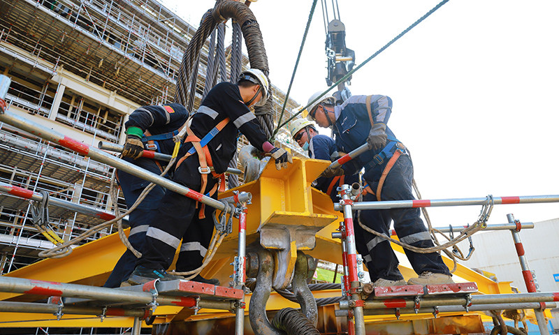 為有效緩解這一局面，高效推動(dòng)項(xiàng)目施工進(jìn)度，建造事業(yè)部青島公司在提升精細(xì)化管理能力和水平上下功夫。通過(guò)成立甲板片臨時(shí)倒運(yùn)小組，提前疏通車道障礙，讓原本滯緩的場(chǎng)地運(yùn)輸工作高效運(yùn)轉(zhuǎn)。圖為Mini E-House（電氣間）吊裝作業(yè)人員合力安裝吊裝鎖具。