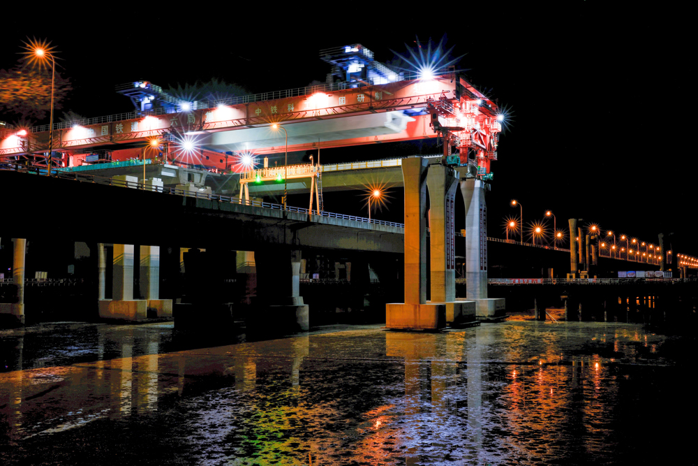 項目團隊圍繞海上50米大跨徑、1800噸超大噸位整孔預制箱梁運輸兩個方面開展科研攻關，研制了我國自主研發、目前世界上最大的公路架橋機“越海號”開展“梁上運架”施工，成功攻克箱梁單體重量大、超高橋面漸變橫坡、高低墩及1800米超小曲線半徑等技術難題，確保了箱梁架設和金塘大橋運營安全，創下了國內采用“梁上運架”技術單體最重的整孔預制箱梁施工紀錄。圖為跨金塘大橋架梁施工現場。