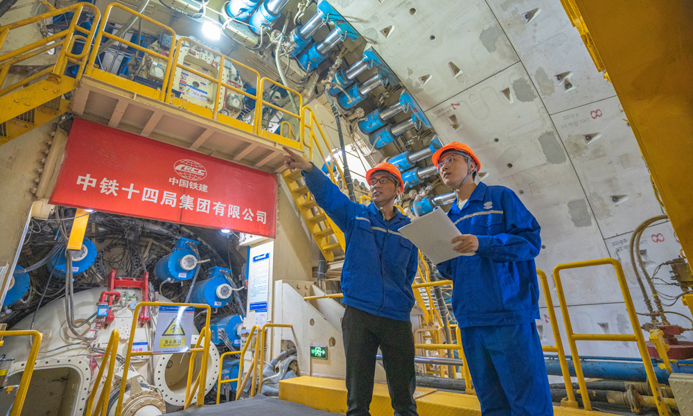 針對(duì)工程特點(diǎn)和項(xiàng)目需求，中鐵十四局對(duì)盾構(gòu)機(jī)進(jìn)行了針對(duì)性設(shè)計(jì)優(yōu)化，聯(lián)合研發(fā)了具有自主知識(shí)產(chǎn)權(quán)的“新穿越號(hào)”盾構(gòu)機(jī)，配置高承壓主驅(qū)動(dòng)密封、大流量泥水沖刷環(huán)流系統(tǒng)、高效物料運(yùn)輸及智能化預(yù)制構(gòu)件同步拼裝技術(shù)、壁后同步注漿密實(shí)度檢測(cè)系統(tǒng)等多項(xiàng)關(guān)鍵技術(shù)，大幅度提高盾構(gòu)機(jī)的適應(yīng)性和可靠性，為工程順利實(shí)施保駕護(hù)航。圖為技術(shù)人員正在檢查“新穿越號(hào)”盾構(gòu)機(jī)的掘進(jìn)狀態(tài)。