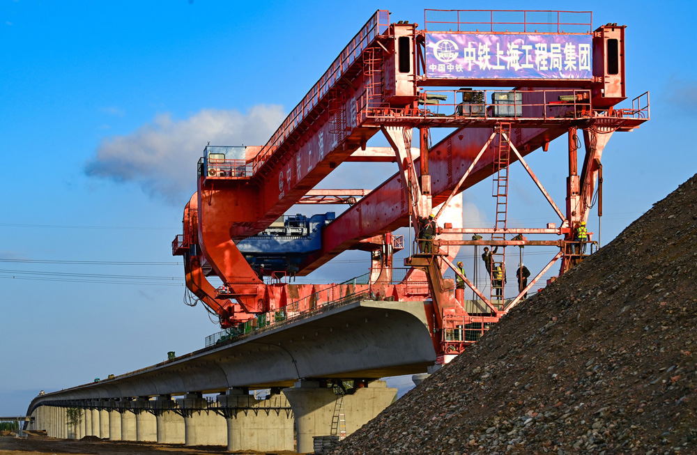 跨萬甘鐵路特大橋全長2526.8米，共有78孔預制箱梁，最大縱坡20‰，運架梁施工過程上跨鐵路且鄰近鐵路營業線，屬于重大危險源管控項目，是包銀高鐵項目重點控制性工程。項目部精心研究制定了運梁、架橋機過孔、架梁專項管理措施和施工方案，全程嚴格盯控架梁施工環節，充分保障了架梁施工安全、質量和進度。圖為包銀高鐵跨萬甘鐵路特大橋箱梁架設施工現場。