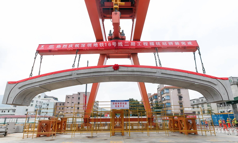 據介紹，福坑站處于巖溶發育區，最大一處溶洞體積近4000立方米，地質條件差，對拼裝時的圍護結構變形控制帶來了巨大的挑戰。該項目大力推進“智能化+信息化+數字化”智能制造平臺建設，通過BIM模型可視化系統等技術應用，實現了集勘察、測量、施工、注漿等于一體的全方位智能化管理。項目組還自主研發了具備旋轉、防搖擺、姿態微調、糾偏等多功能“180噸門式起重機+分離式拼裝臺車”工裝設備，實現了梁、板、柱、墻等預制構件的吊裝、翻轉、旋轉等姿態調整，達到了毫米級的精準拼裝。圖為最后一塊頂板吊裝。