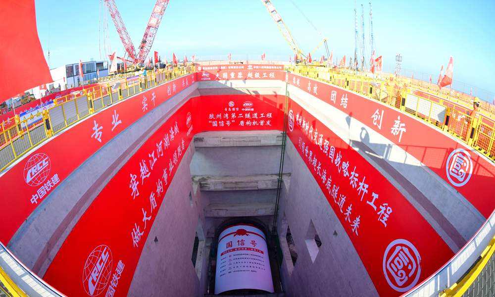 6月30日，膠州灣第二隧道“國信號”盾構機在青島港8號碼頭順利首發，標志著由青島國信集團投資建設，中國鐵建所屬鐵四院設計、中鐵十四局施工的世界最長海底道路隧道——膠州灣第二隧道工程盾構段正式掘進施工，開啟了膠州灣東西兩岸“對向掘進”的跨海征途。圖為膠州灣第二隧道“國信號”盾構機始發現場。