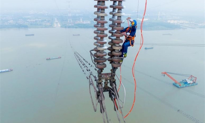 國家電網江蘇南京供電公司工作人員在500千伏汊龍汊王線跨江高塔上使用高壓泵給絕緣子噴涂防污閃涂料，提高其絕緣性能。