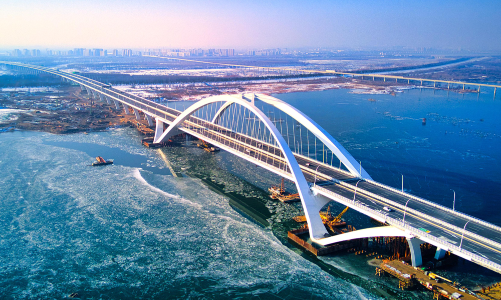 京雄高速公路（北京段）自2020年12月開工建設以來，中國中鐵建設者綜合利用30余項專利技術優勢，先后攻克“筑造精品工程、建設周期保障、危大工程管控、征拆難點破解、關鍵技術攻堅”五大重難點。全長1.62公里的京雄大橋是國內首座空間異形拱肋飛燕提籃式鋼箱拱橋，是北京地區單跨跨度最大橋梁，通過運用數字化孿生技術，采用異形曲面拱肋數字化加工制造、拱肋吊裝支架監測等新技術，極大提升了工程建造品質。房山北站是北京市首座陸地高架橋主線收費站，創新性采用橋梁分幅設計，將快慢車、客貨車進行分離式指引通行，將大幅提升通行效率。圖為京雄高速公路京雄大橋。