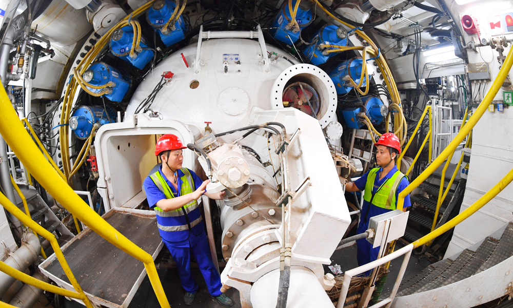 據(jù)介紹，隧道最大埋深53米，連續(xù)穿越密集建構(gòu)筑物和珠江多個水道，地質(zhì)條件復(fù)雜，周邊交通繁忙，施工難度大、管理要求高。項目團隊在盾構(gòu)機進(jìn)行了針對性設(shè)計，配備伸縮式主驅(qū)動、伸縮攝像頭、自動測量監(jiān)控系統(tǒng)、刀具磨損檢測等多項創(chuàng)新技術(shù)。施工中采取“原位保護(hù)”、樁基托換等，實現(xiàn)了歷史保護(hù)建筑毫米級沉降控制，最快月掘進(jìn)324米，創(chuàng)造我國華南地區(qū)復(fù)合地層超大直徑泥水盾構(gòu)掘進(jìn)紀(jì)錄。圖為技術(shù)人員檢查盾構(gòu)機工作狀態(tài)。