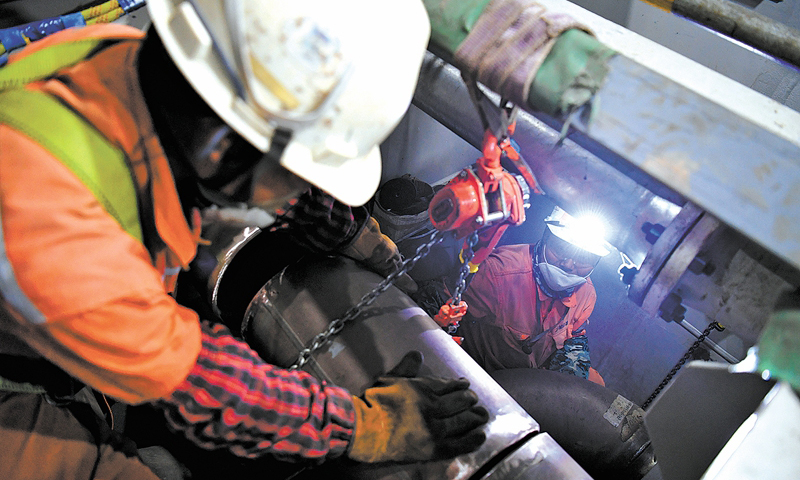 6月29日早7時(shí)許，滂沱大雨中，霧氣籠罩的中國海油青島場地上，陵水17-2半潛平臺船體四條“擎天巨臂”的最后一個(gè)“關(guān)節(jié)”完成吊裝。至此，我國首個(gè)1500米深水半潛平臺船體提前16天完成結(jié)構(gòu)封頂，為船體陸地建造完工贏得了寶貴的時(shí)間。圖為船體內(nèi)部，作業(yè)人員進(jìn)行管線對接作業(yè)。