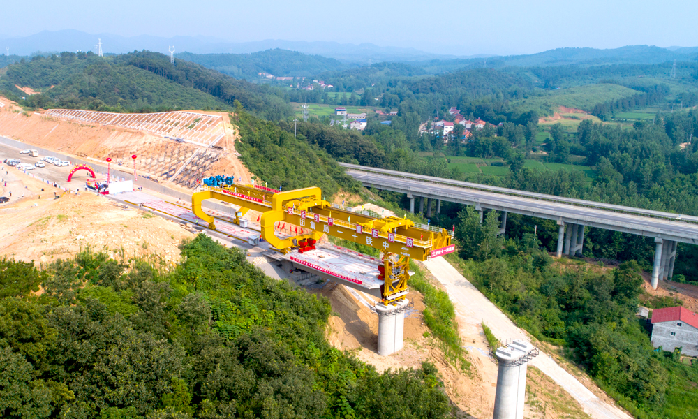 7月22日上午，鄭（州）萬（州）高鐵最難施工段——湖北段ZWZQ-5標首榀箱梁架設(shè)成功，標志著鄭萬高鐵全面進入架梁階段。當日，由中鐵十一局漢江重工自行研制的新型900噸級梁架橋機，在施工人員操控下，將一榀長24米、寬12.6米、高3.035米、重600噸的箱梁平穩(wěn)精準安放在橋墩上，至此，標志鄭萬高鐵最難施工段已達到架梁標準，架梁施工步入正軌。